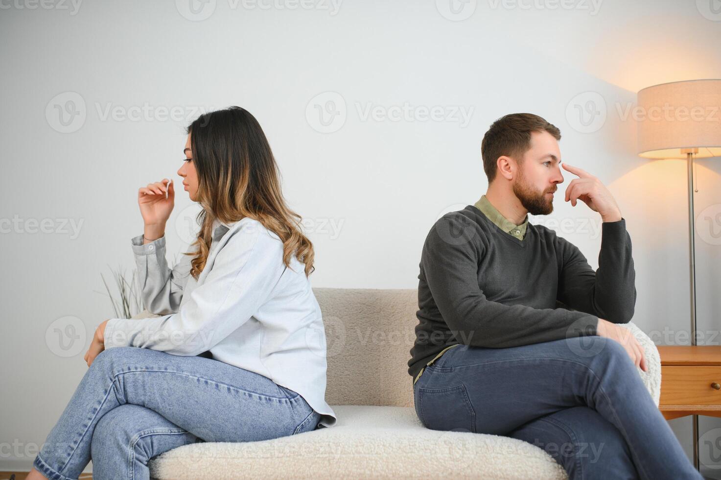 Beautiful couple is sitting back to back on the couch while having a quarrel photo