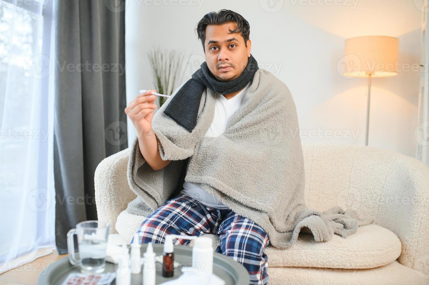 health, cold and people concept - sick young indian man in blanket having headache or fever at home photo