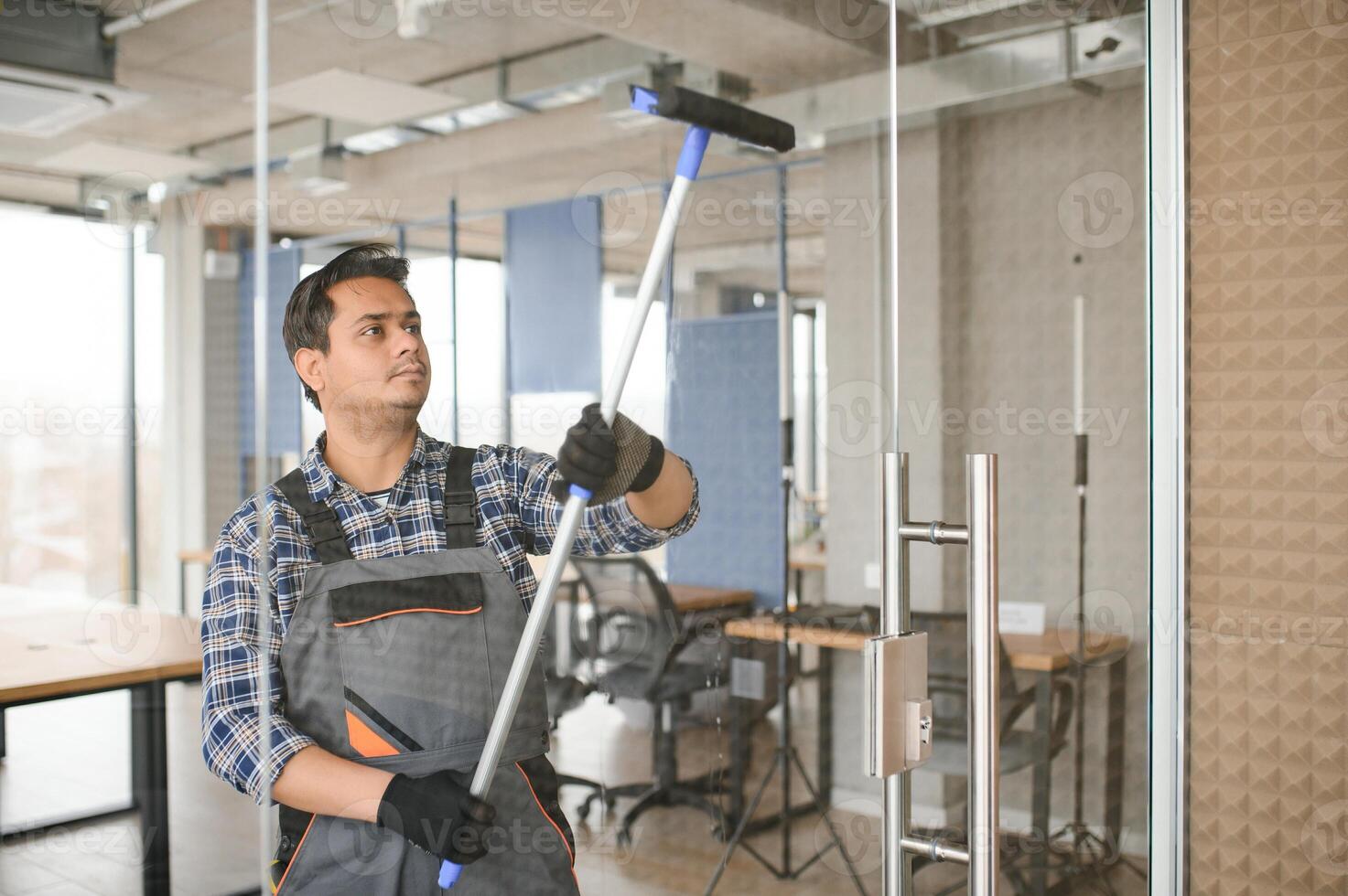 Male janitor cleaning window in office photo