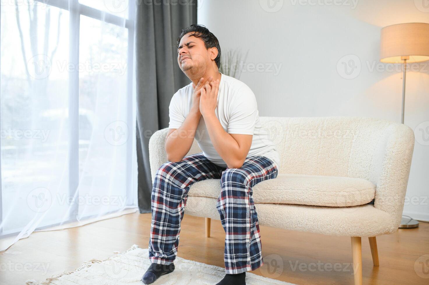 Sick young indian man suffering throat ache while sitting on bed at home photo