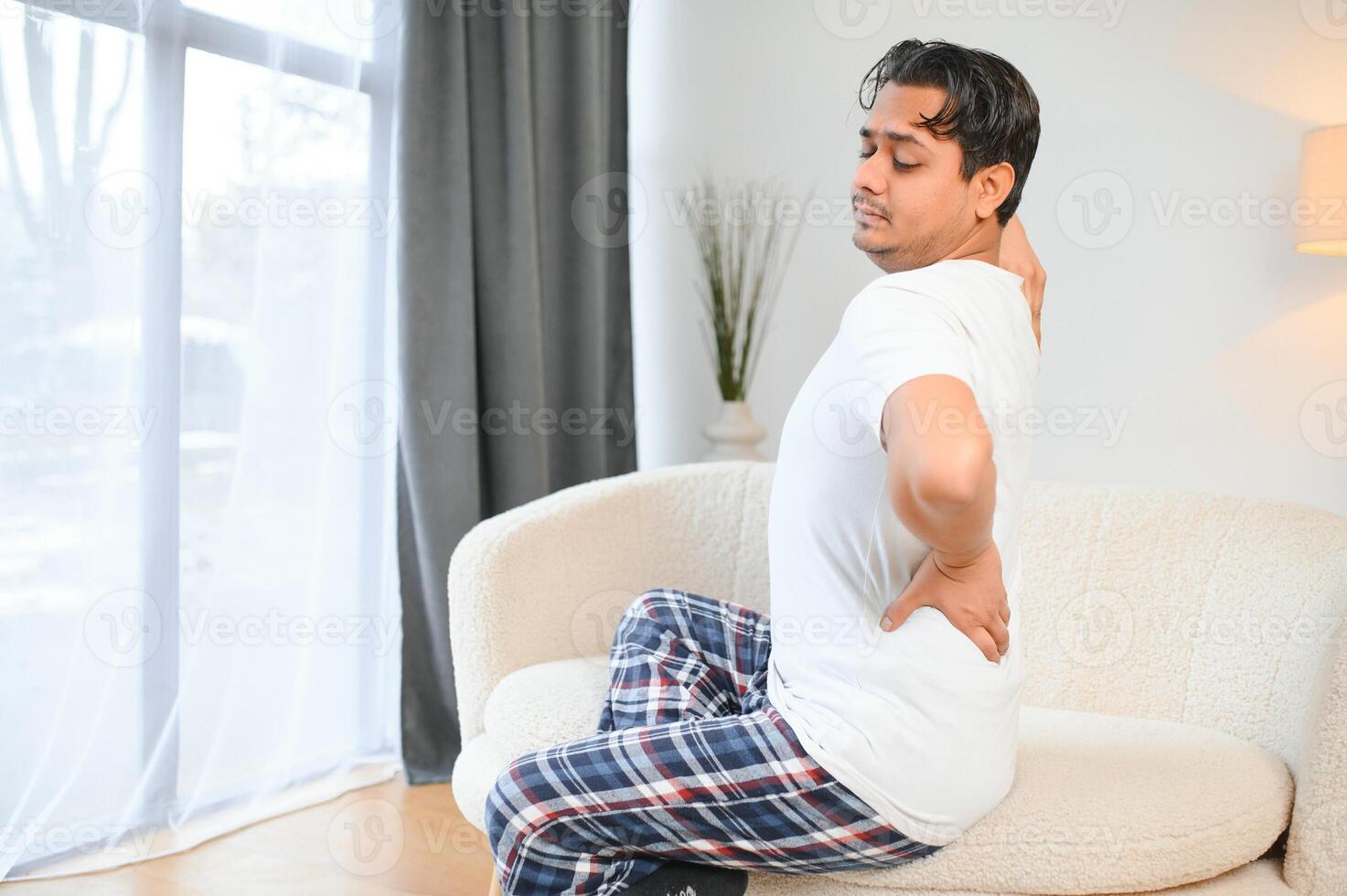 A sick man on Christmas has severe back pain, massages muscle his hand sitting on sofa in living room photo