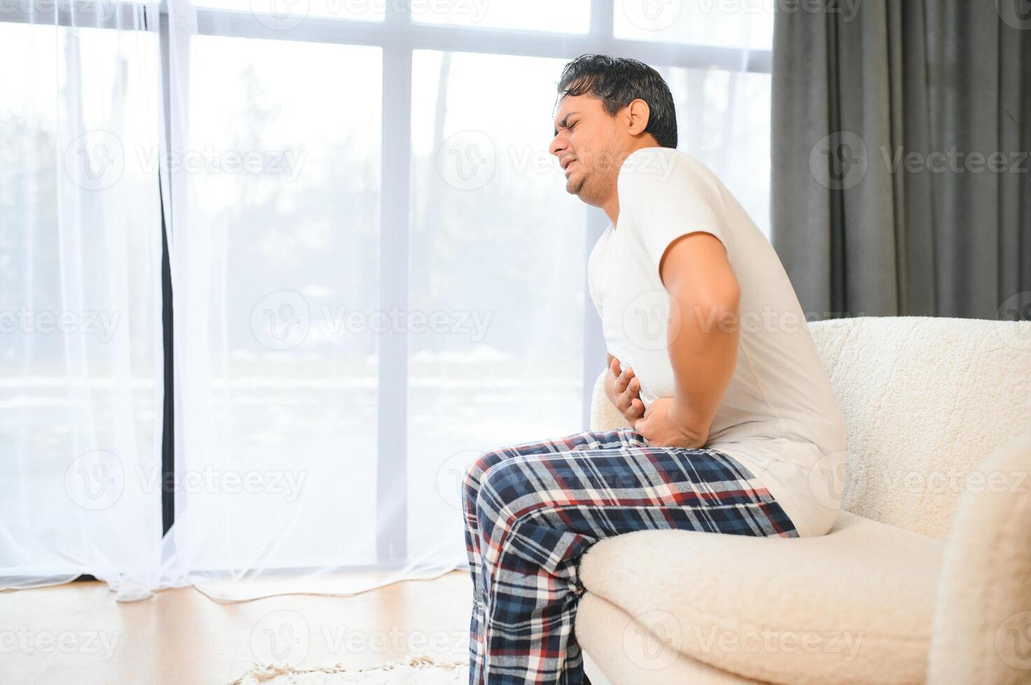 Sad exhausted guy of indian and arabian ethnicity, holds his hands on his stomach, grimaces from pain in his stomach, suffers from poisoning, spasm, stomach problems photo