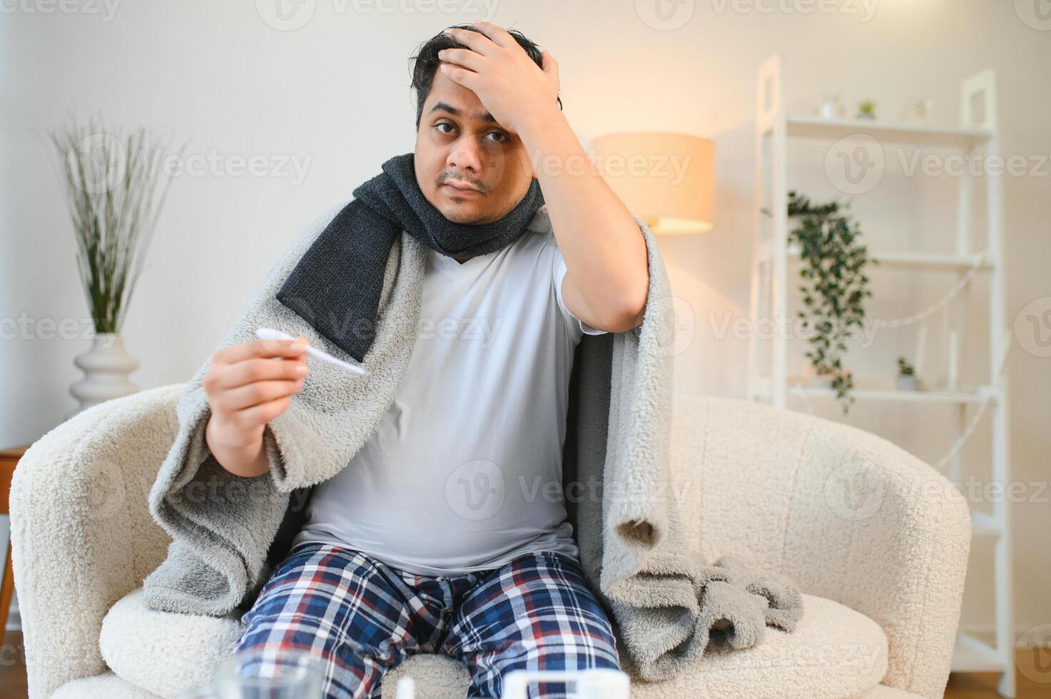 health, cold and people concept - sick young indian man in blanket having headache or fever at home photo