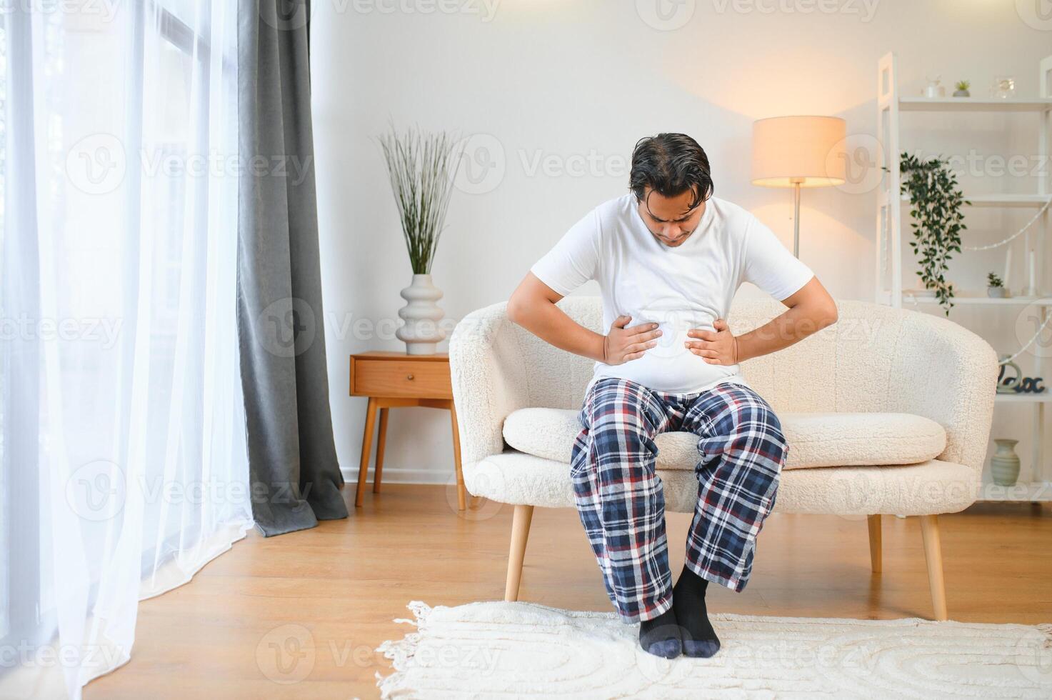 Sad exhausted guy of indian and arabian ethnicity, holds his hands on his stomach, grimaces from pain in his stomach, suffers from poisoning, spasm, stomach problems photo