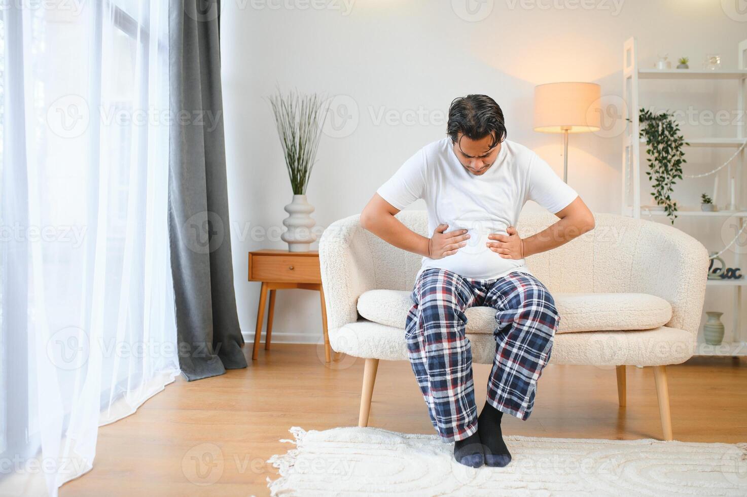 triste agotado chico de indio y árabe etnicidad, sostiene su manos en su estómago, muecas desde dolor en su estómago, sufre desde envenenamiento, espasmo, estómago problemas foto