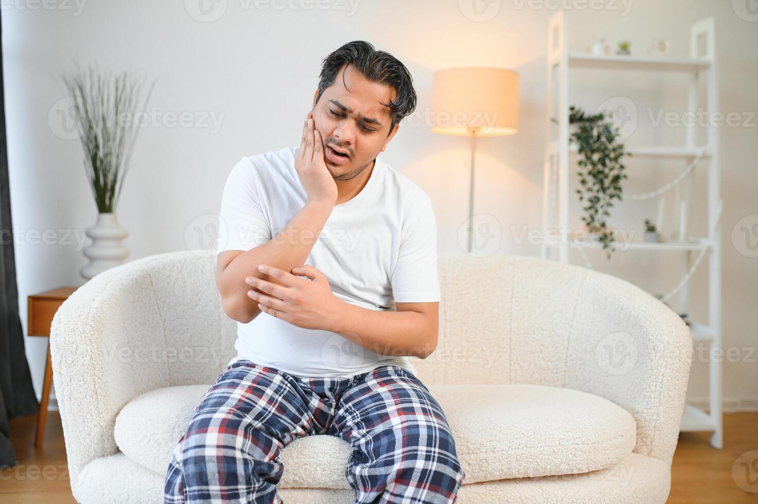 Sad exhausted guy of indian and arabian ethnicity, holds his hands on his stomach, grimaces from pain in his stomach, suffers from poisoning, spasm, stomach problems photo