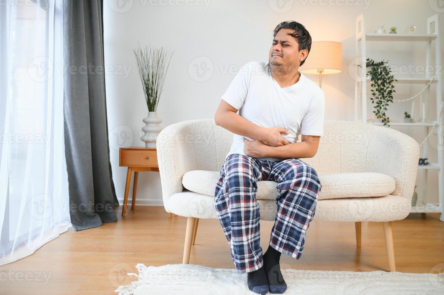 Sad exhausted guy of indian and arabian ethnicity, holds his hands on his stomach, grimaces from pain in his stomach, suffers from poisoning, spasm, stomach problems photo