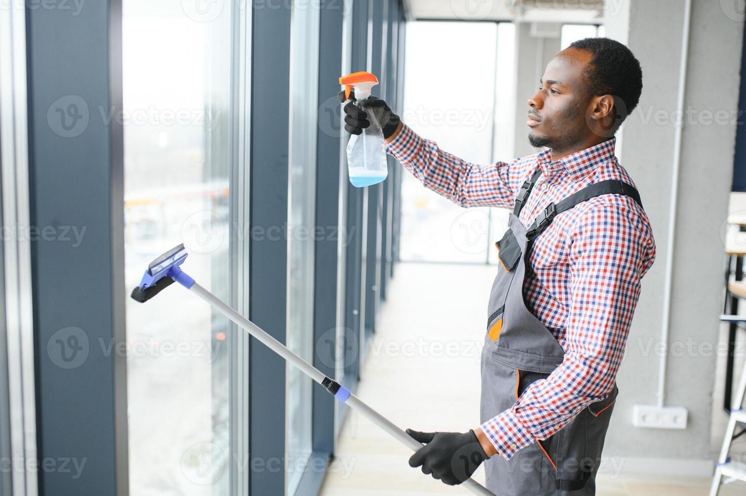 African Male professional cleaning service worker in overalls cleans the windows and shop windows of a store with special equipment photo