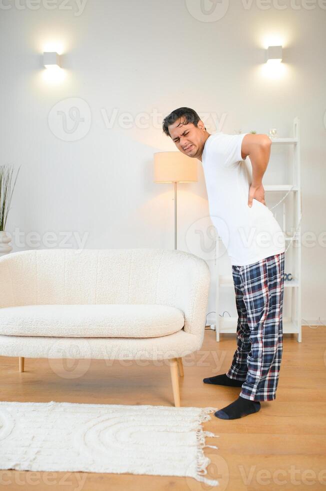 Portrait of Indian guy backache, holding spine with hand photo