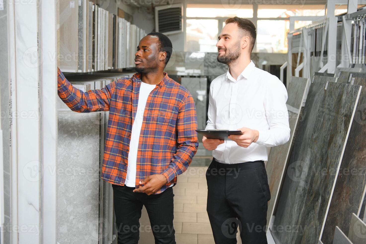 African man choosing ceramic tiles and utensils for his home bathroom and male seller helps him to make right decision photo