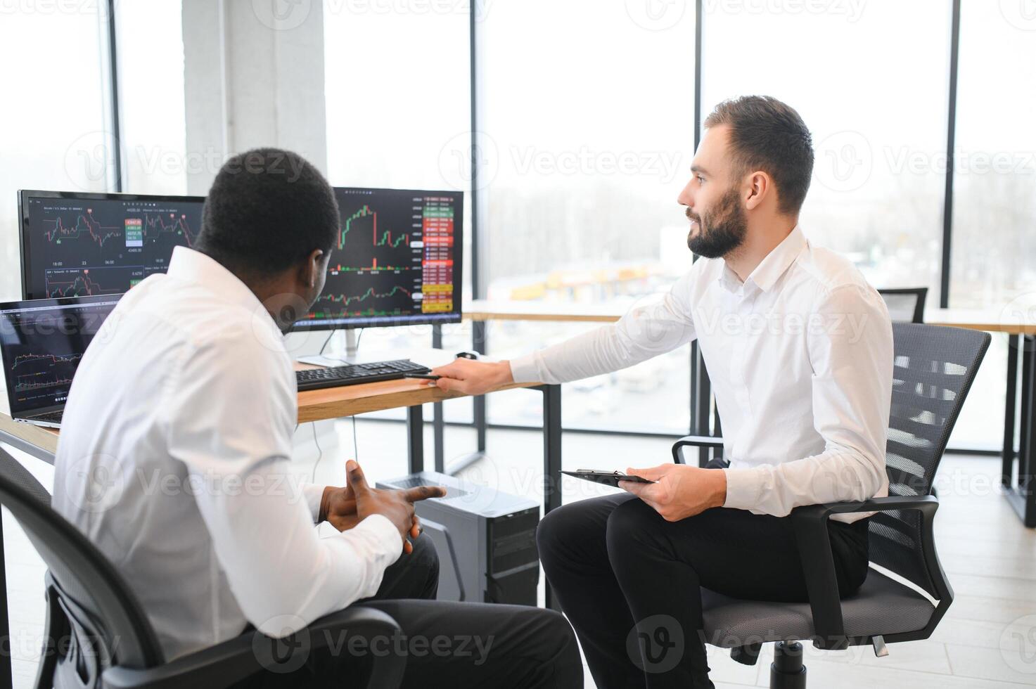 dos diverso colegas comerciantes hablando a cada otro, sentado en el oficina en frente de múltiple computadora pantallas valores comercio, gente, negocio concepto foto