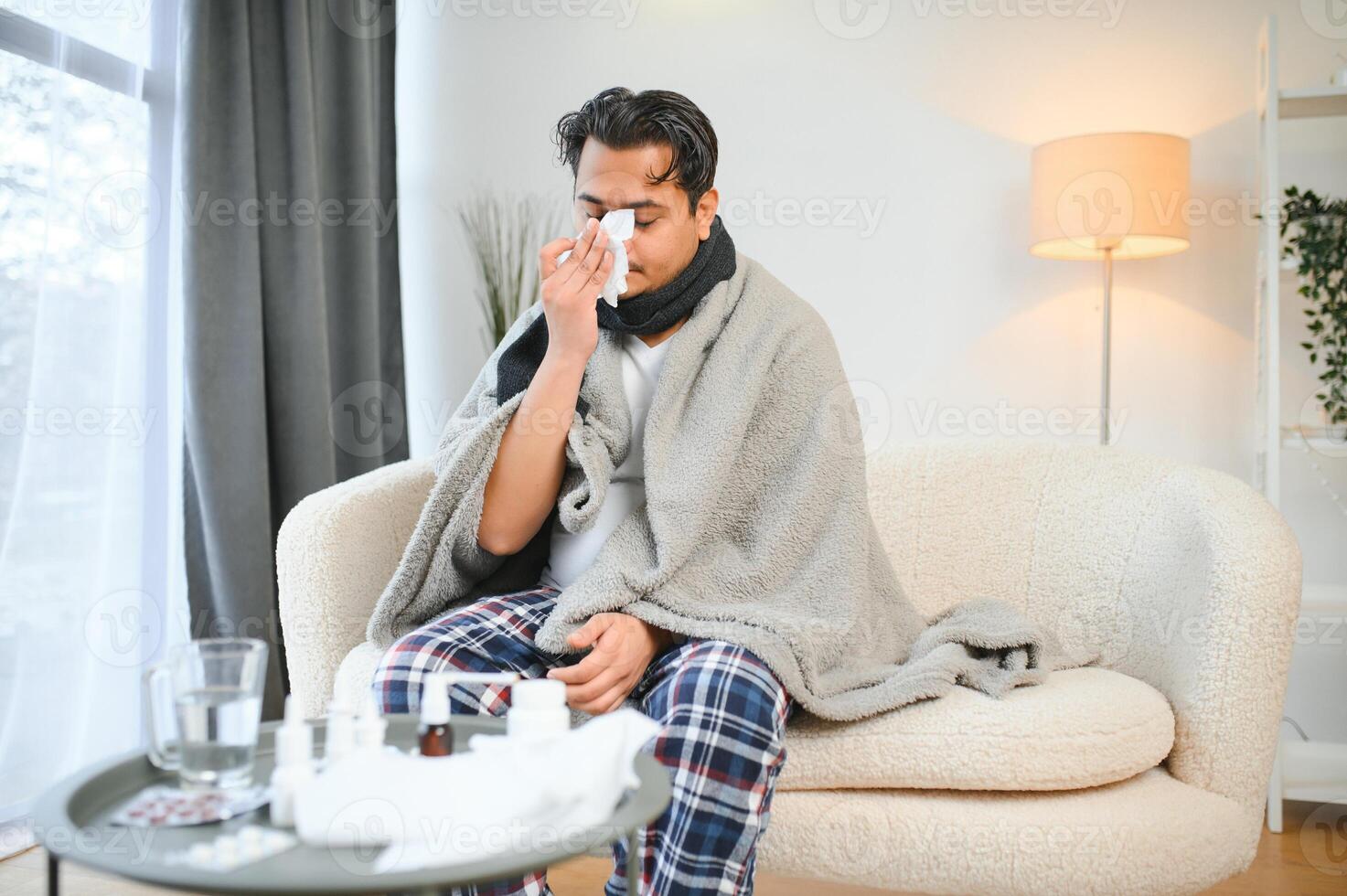 health, cold and people concept - sick young indian man in blanket having headache or fever at home photo