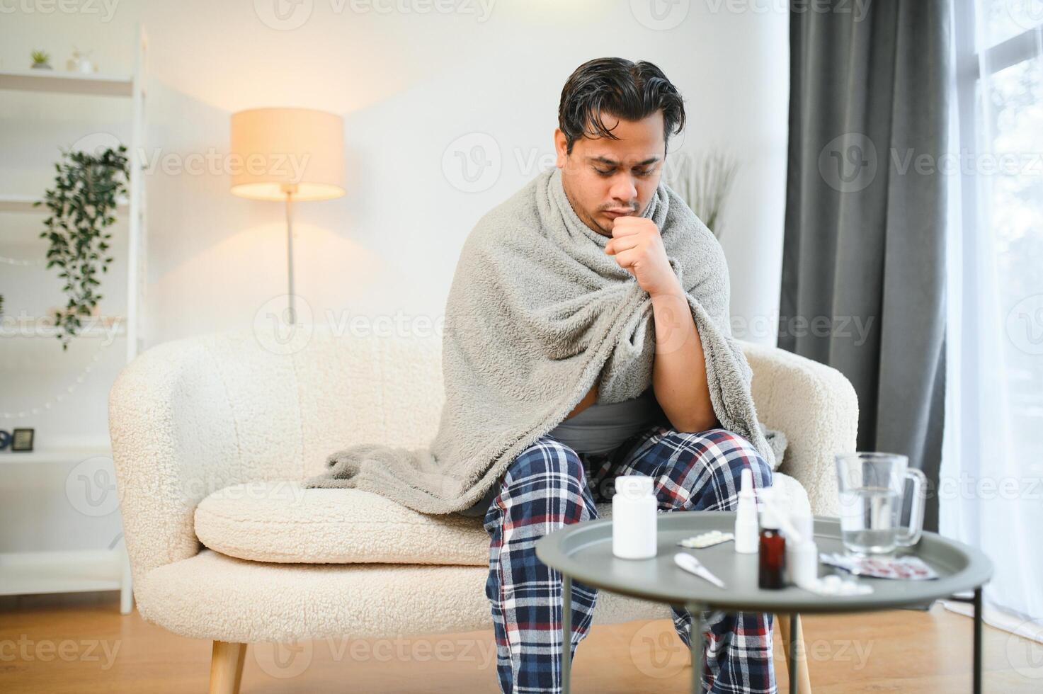 Sick Indian man in plaid sit alone shivering from cold. Unhealthy Arabian guy sit on chair feeling discomfort try to warming up photo