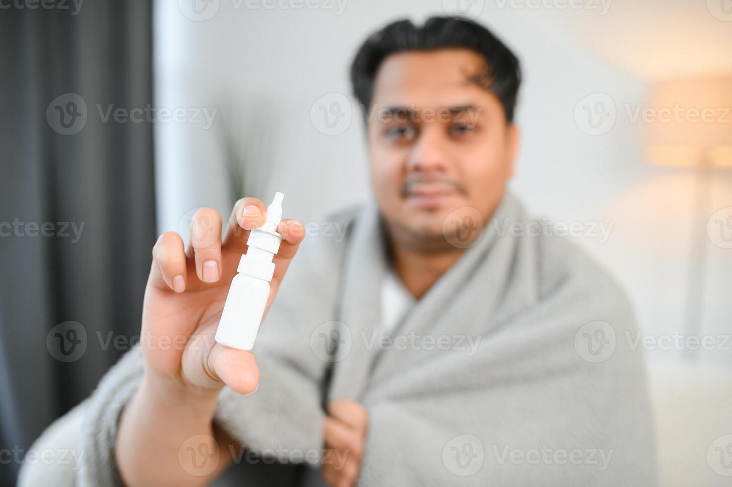 A sick Indian is treated at home and uses a nasal spray. Healthcare concept photo