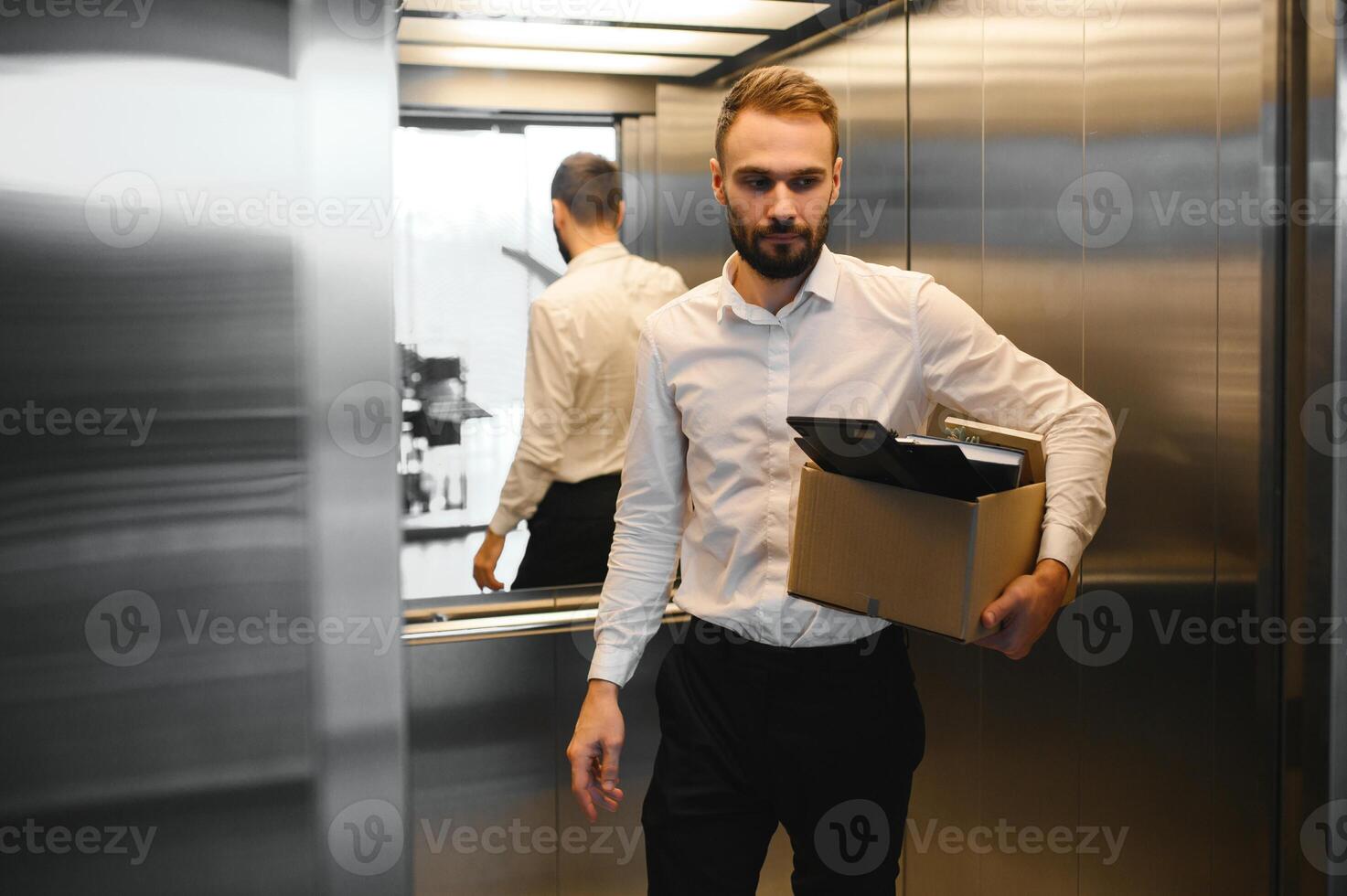 Young handsome businessman in light modern office with carton box. Last day at work. Upset office worker is fired photo