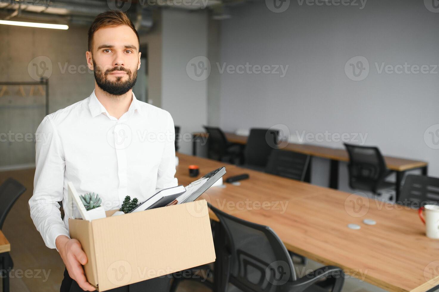 joven hermoso empresario en ligero moderno oficina con caja de cartón caja. último día a trabajar. trastornado oficina trabajador es despedido foto