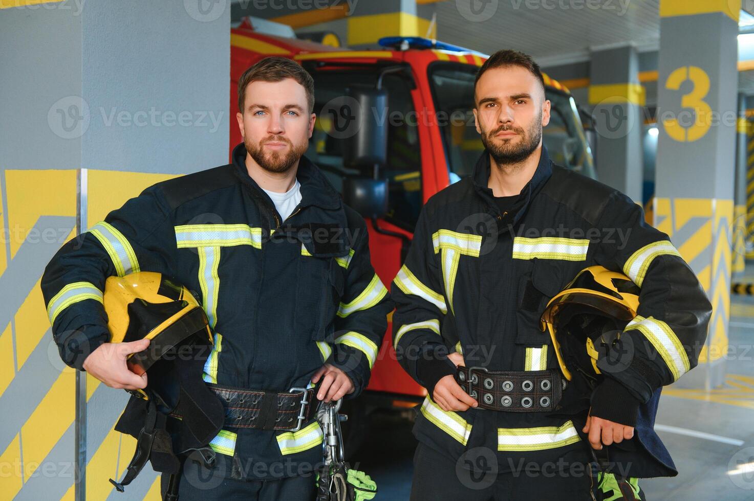 Portrait of two young firemen in uniform standing inside the fire station photo