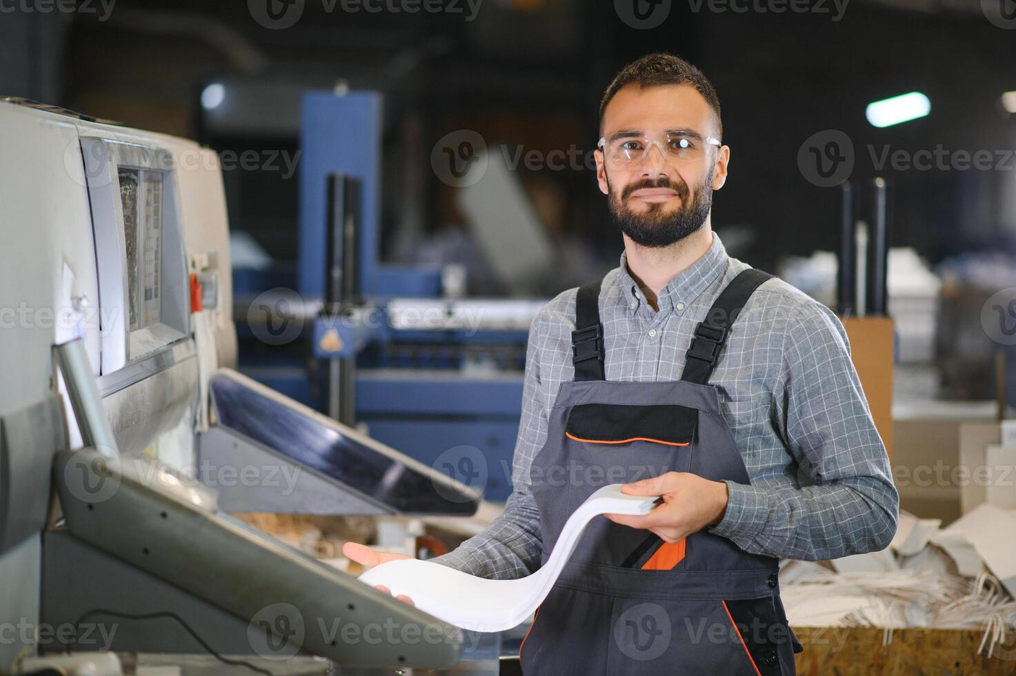 Printing house interior with modern offset print machine and operator in working uniform checking quality and controlling process of print photo