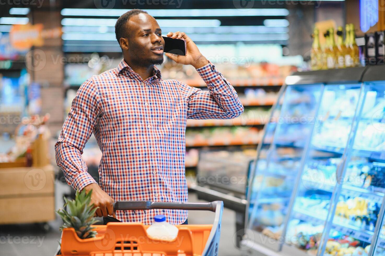 African American Man Talking On Cellphone Chatting While Shopping Groceries In Supermarket photo