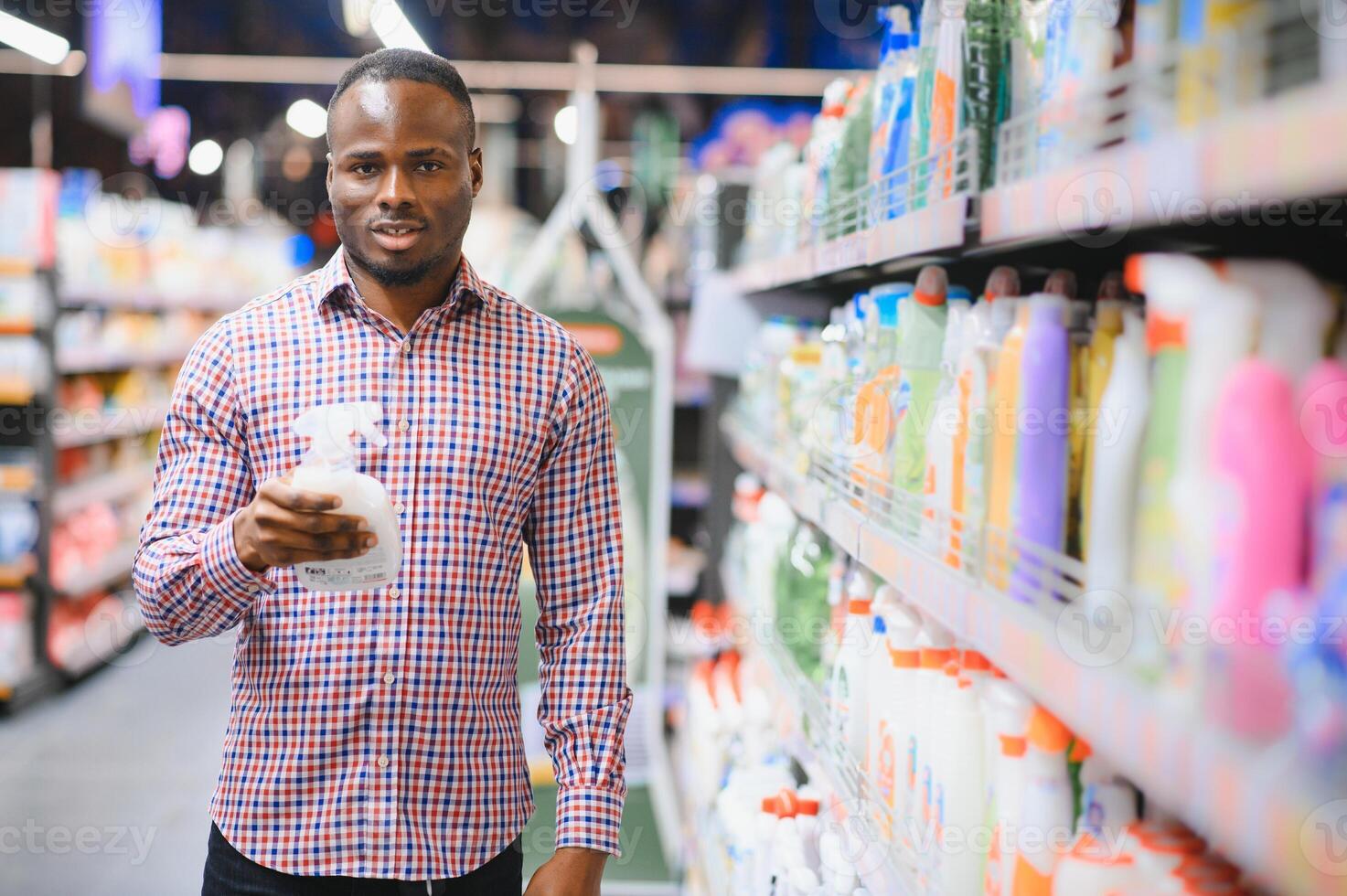 African man holding bottle of household chemicals in big store photo