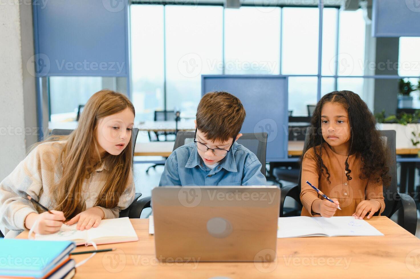 Portrait of smart schoolgirls and schoolboys looking at the laptop in classroom photo