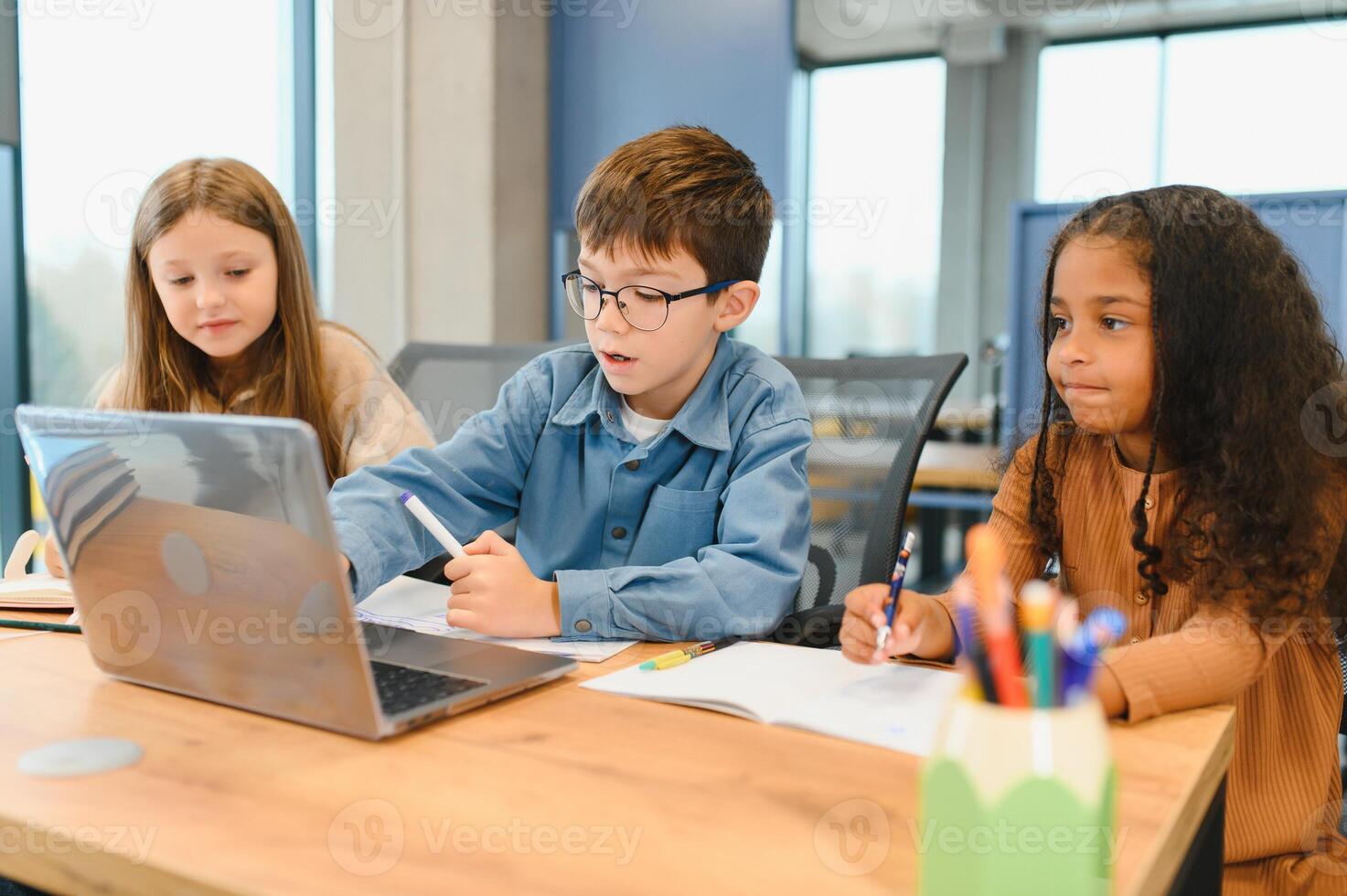 Portrait of smart schoolgirls and schoolboys looking at the laptop in classroom photo