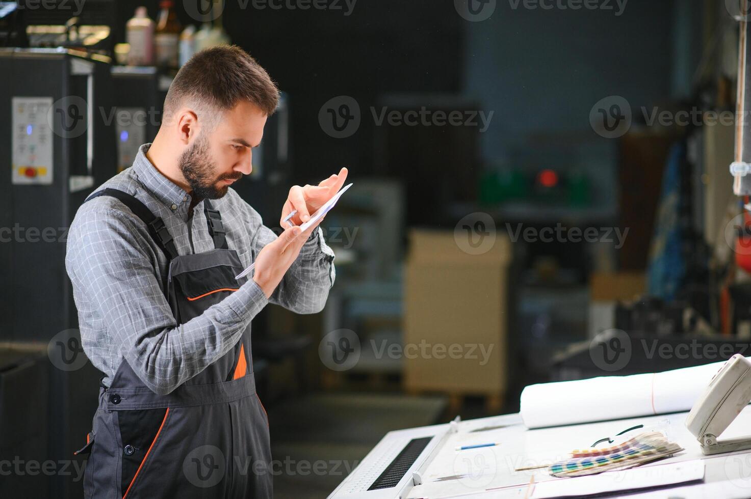 Print house worker controlling printing process quality and checking colors with magnifying glass photo