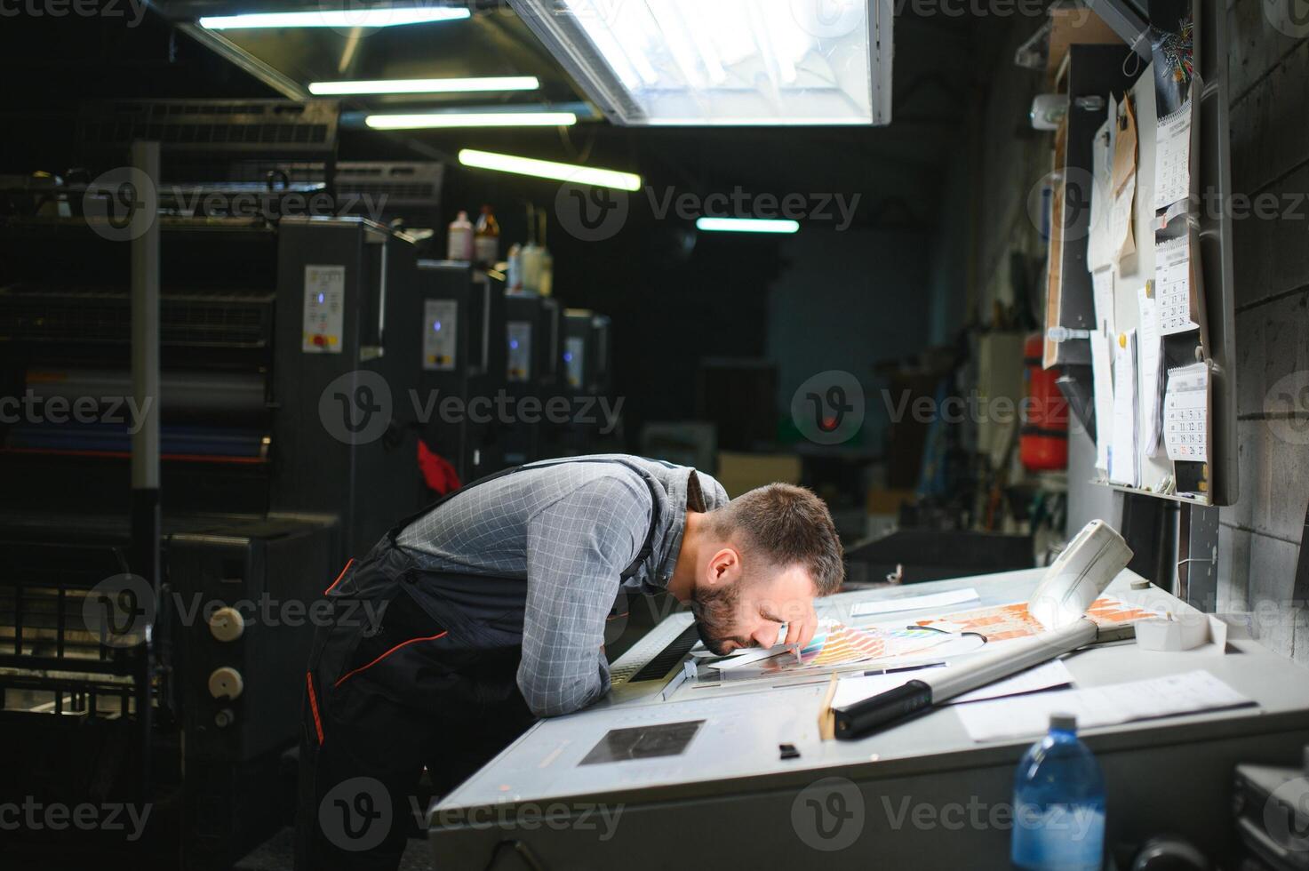 Print house worker controlling printing process quality and checking colors with magnifying glass photo