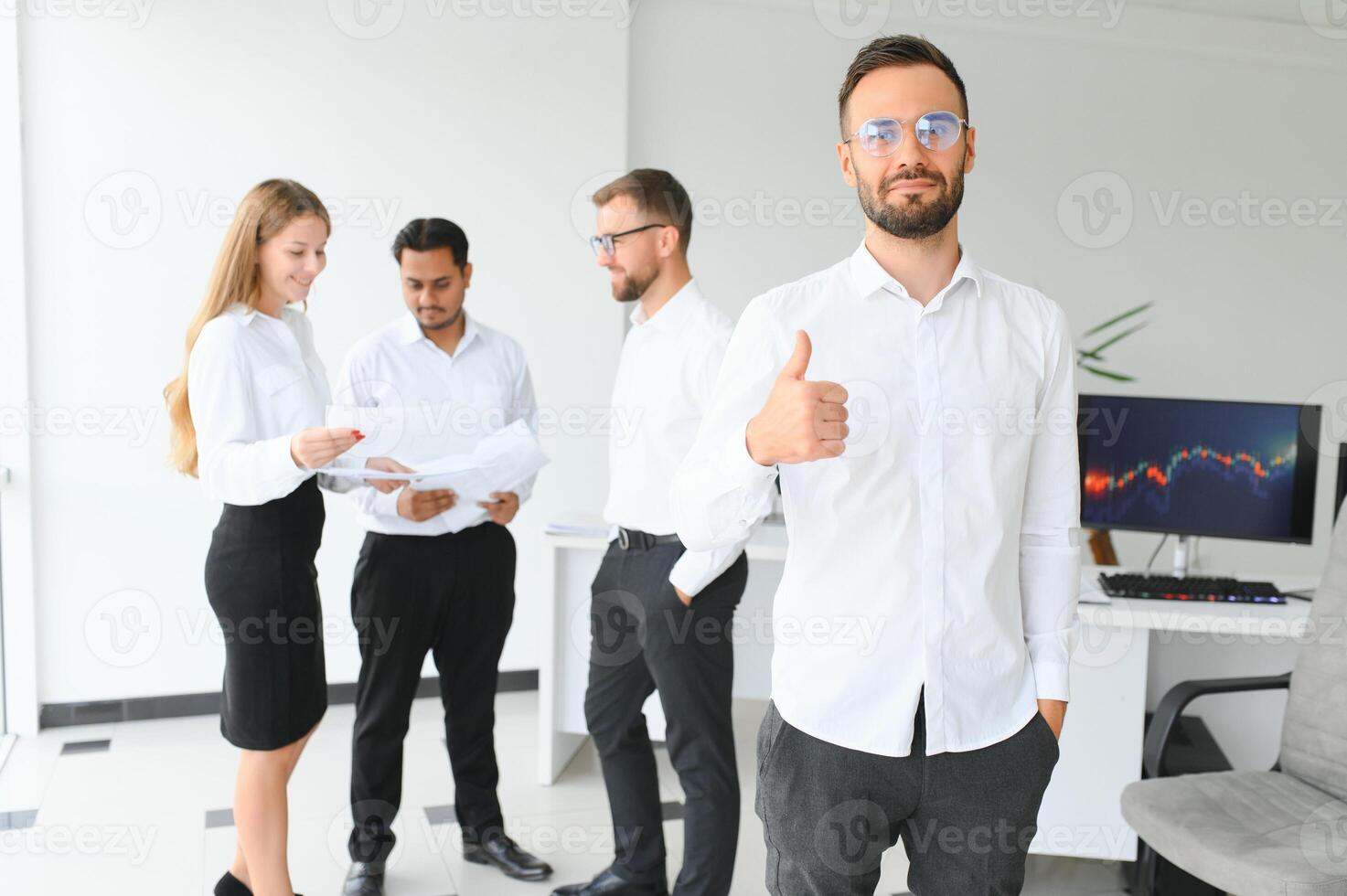 Team leader stands with coworkers in background photo