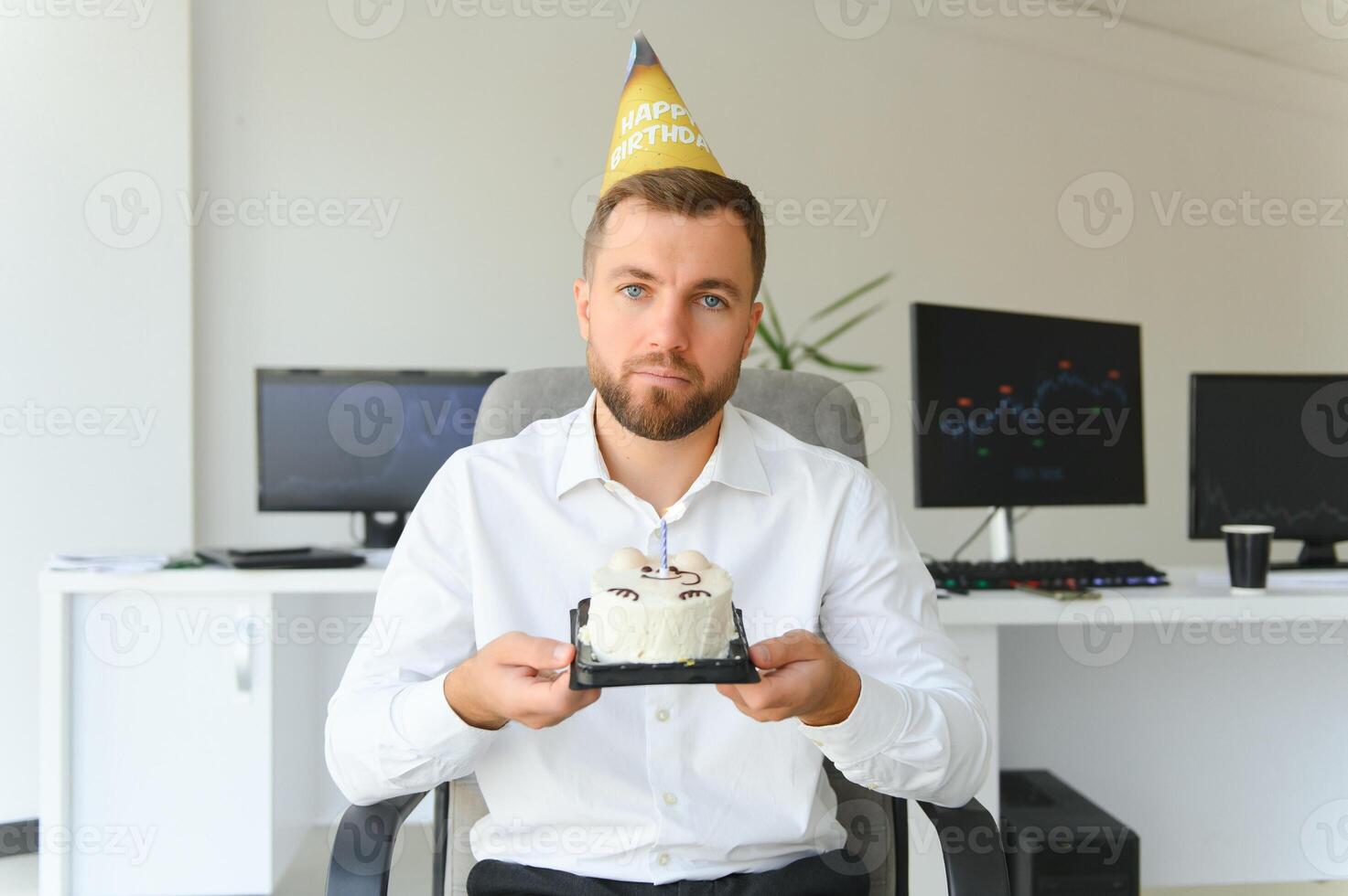 Sad young businessman celebrating birthday alone in office photo