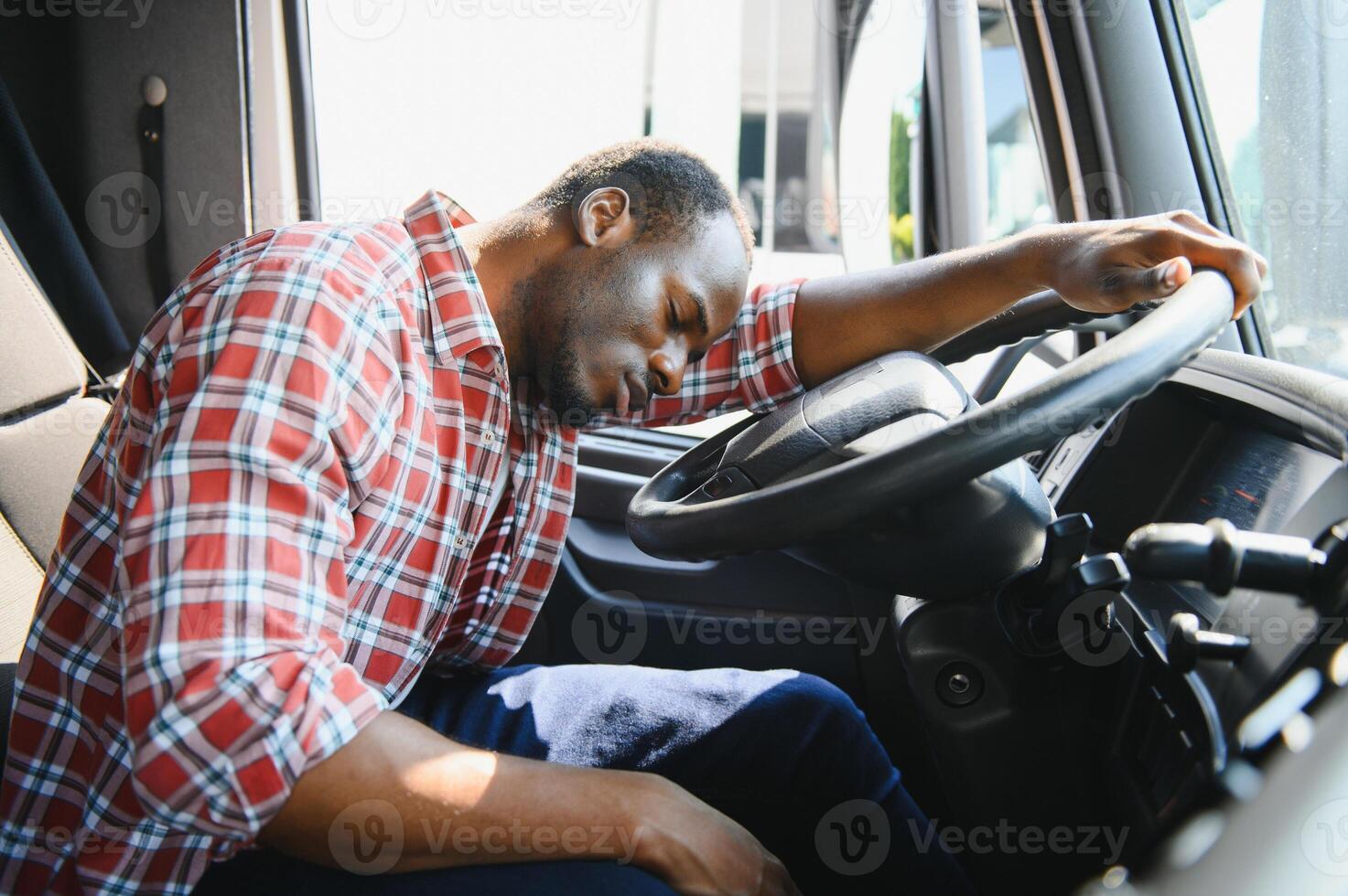 Tired of work. Sitting in the cabin. Young african american truck driver is with his vehicle at daytime. photo