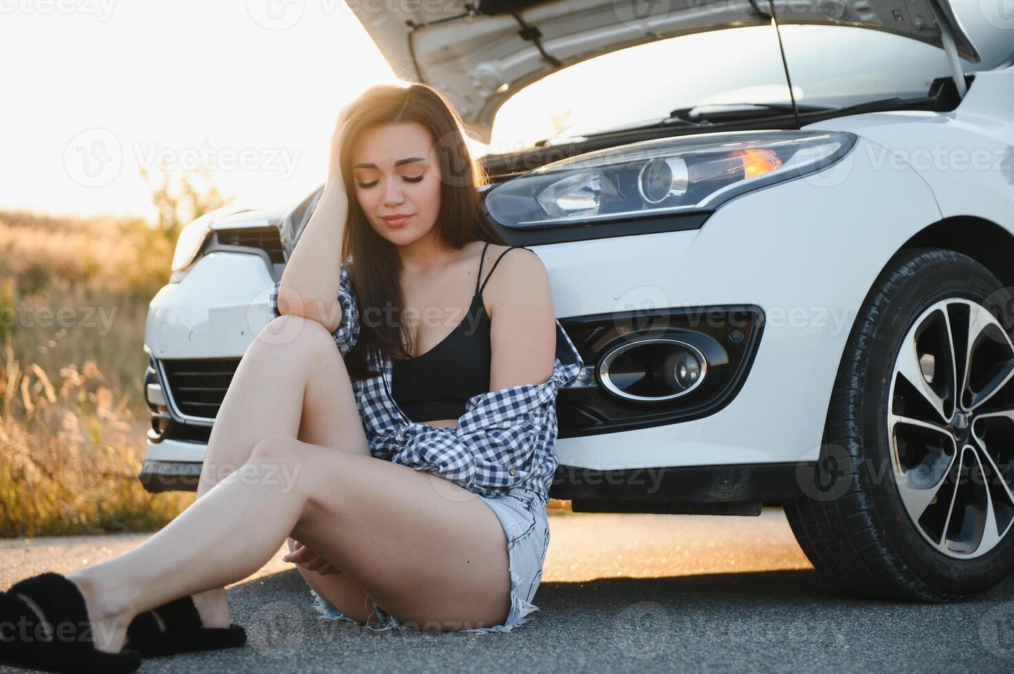 hermosa joven niña sentado a un roto coche en el la carretera desesperado a obtener ayuda foto