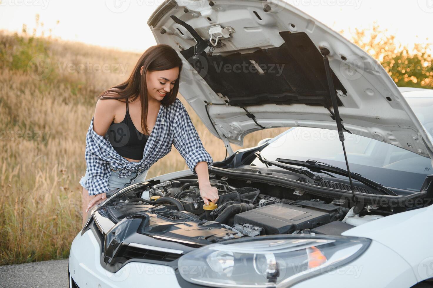 hermosa Delgado niña en camisa y pantalones cortos mira en abierto coche capucha en un la carretera foto