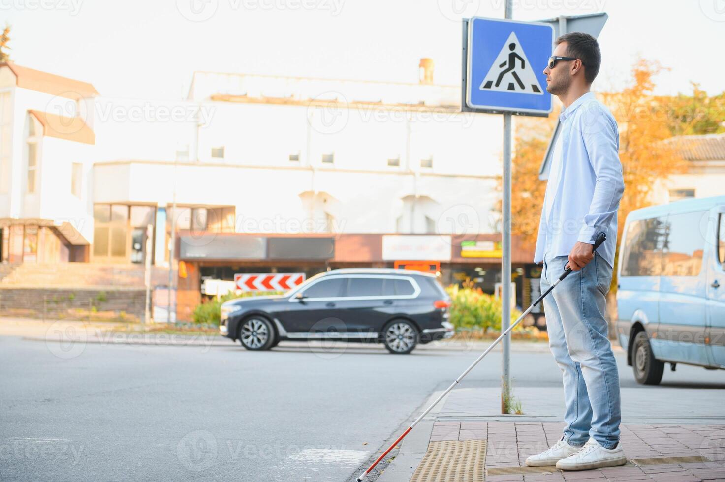 Young handsome blinded man walking with stick in town photo