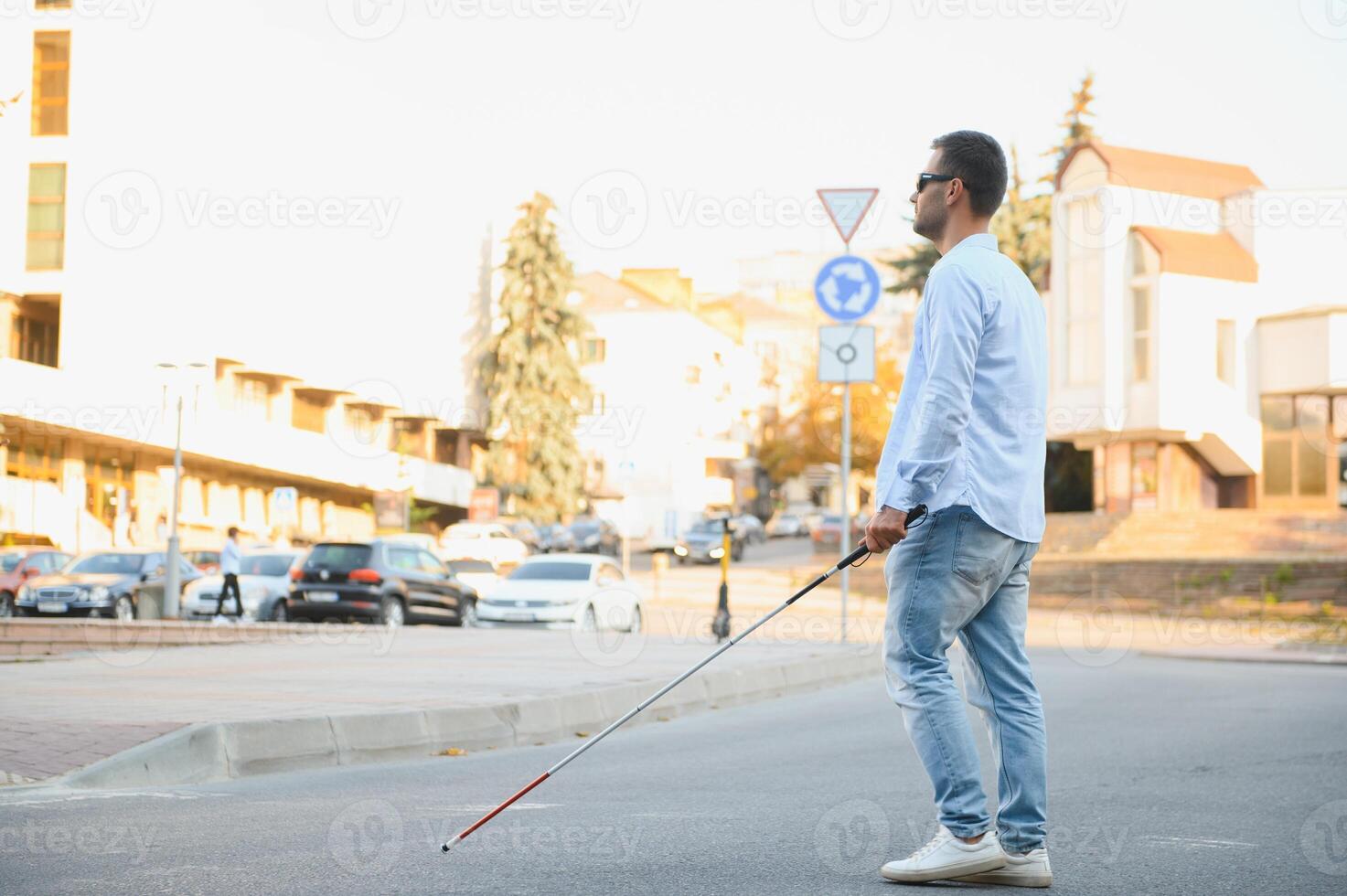 Young handsome blinded man walking with stick in town photo