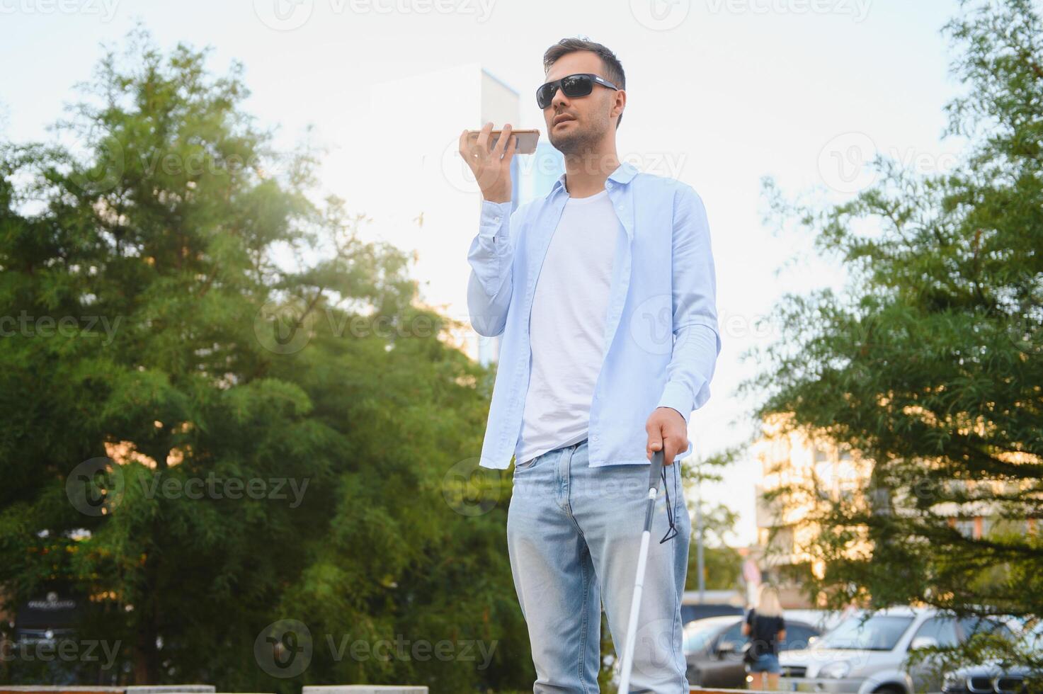 Young blind man with smartphone in city, calling photo