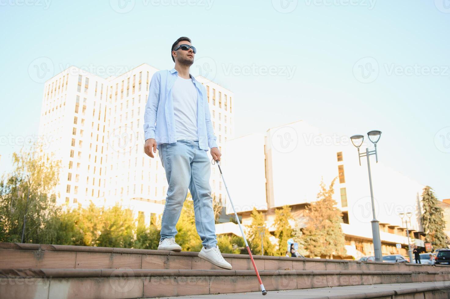 Young handsome blinded man walking with stick in town photo