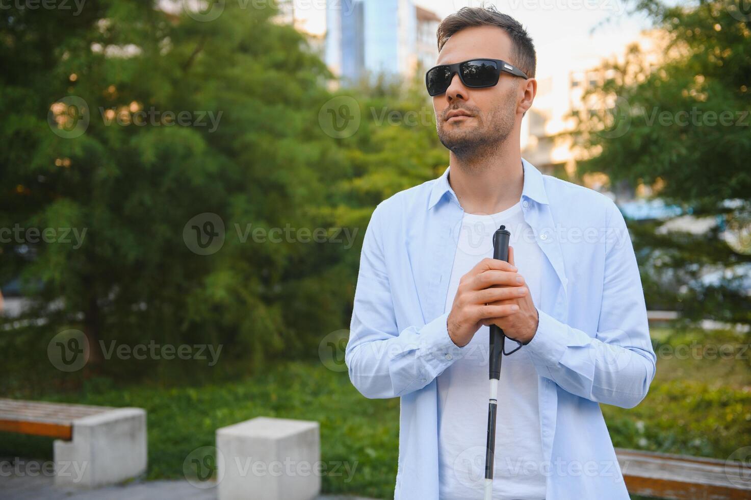 Young handsome blinded man walking with stick in town photo
