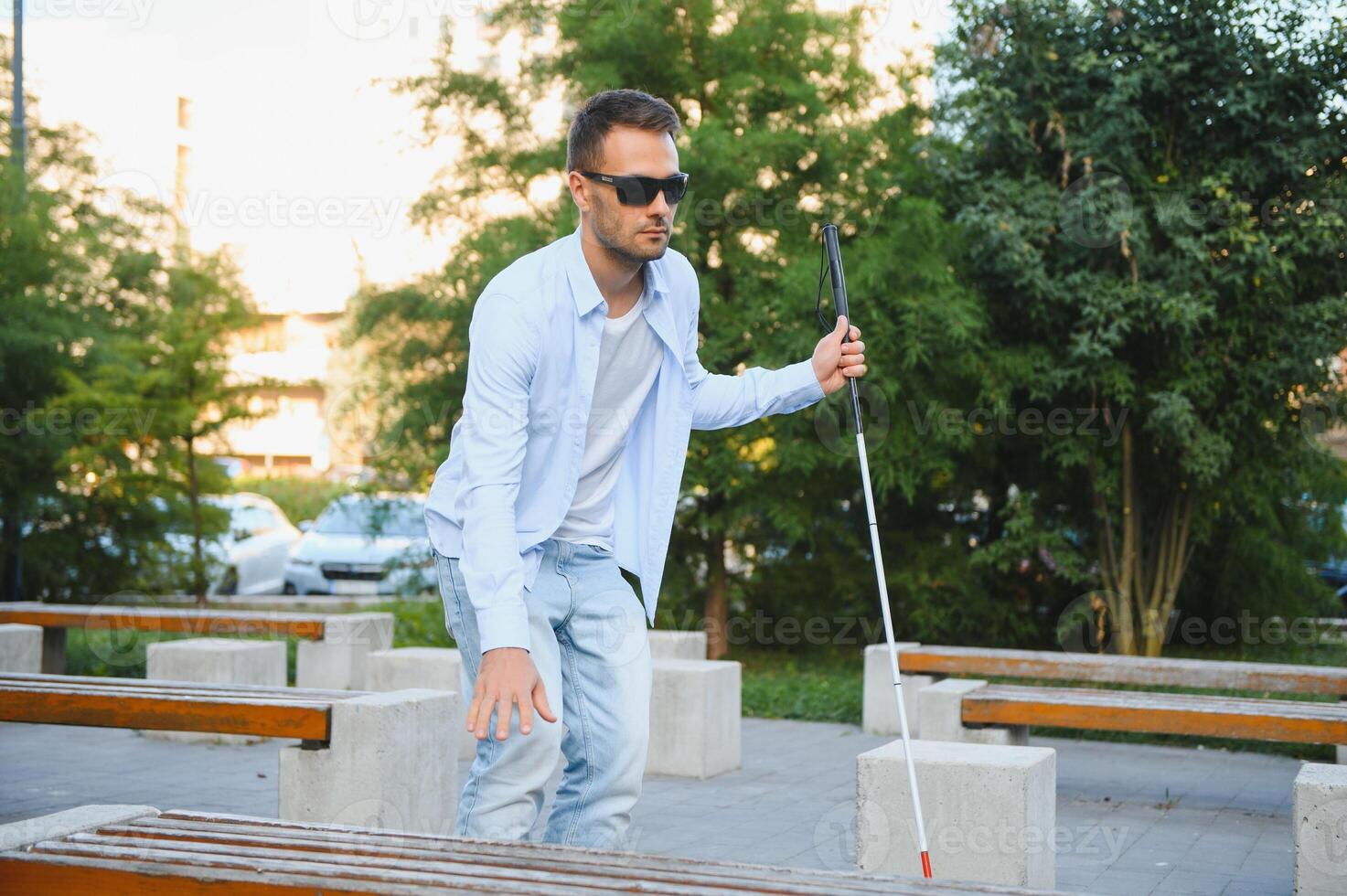 Young handsome blinded man walking with stick in town photo