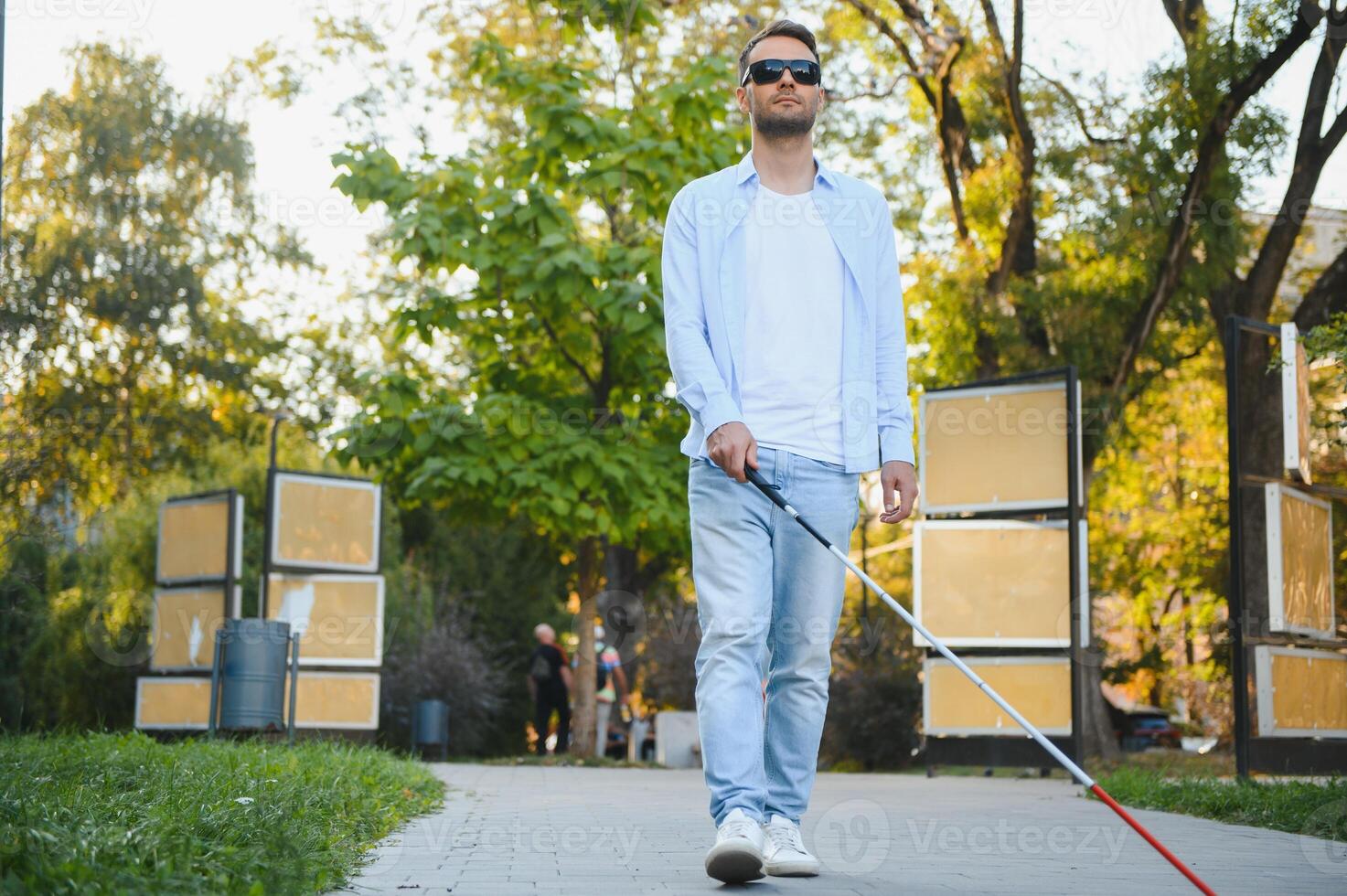 Young handsome blinded man walking with stick in town photo