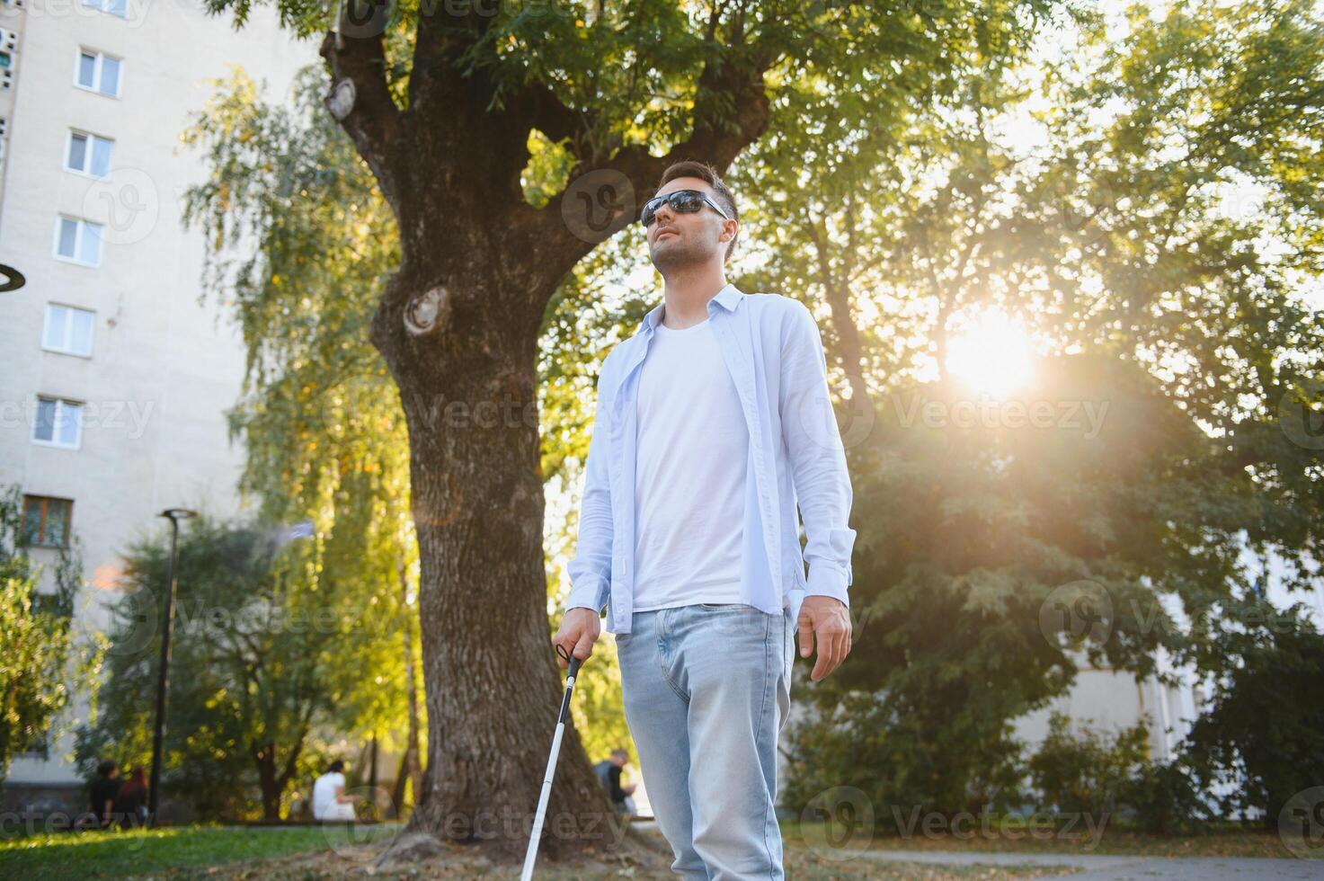 Young handsome blinded man walking with stick in town photo