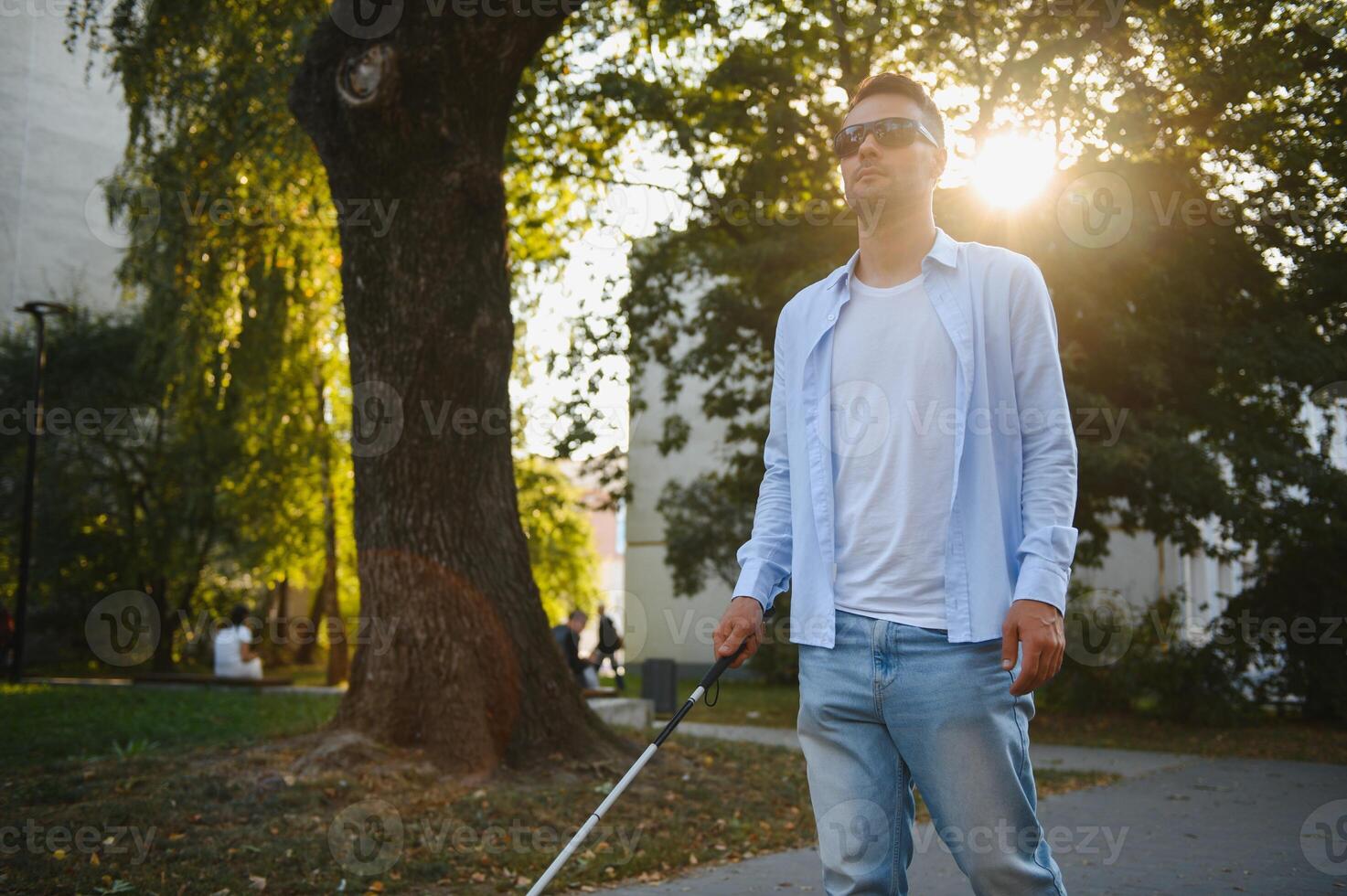 Young handsome blinded man walking with stick in town photo