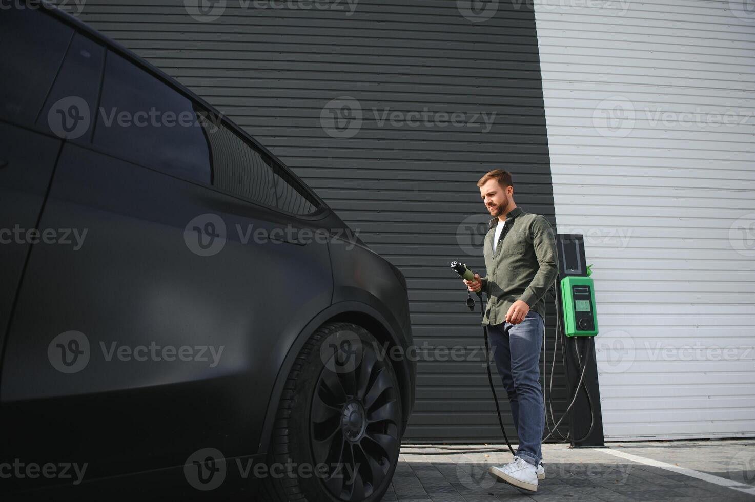 A man stands near a charging station and charges his electric car photo