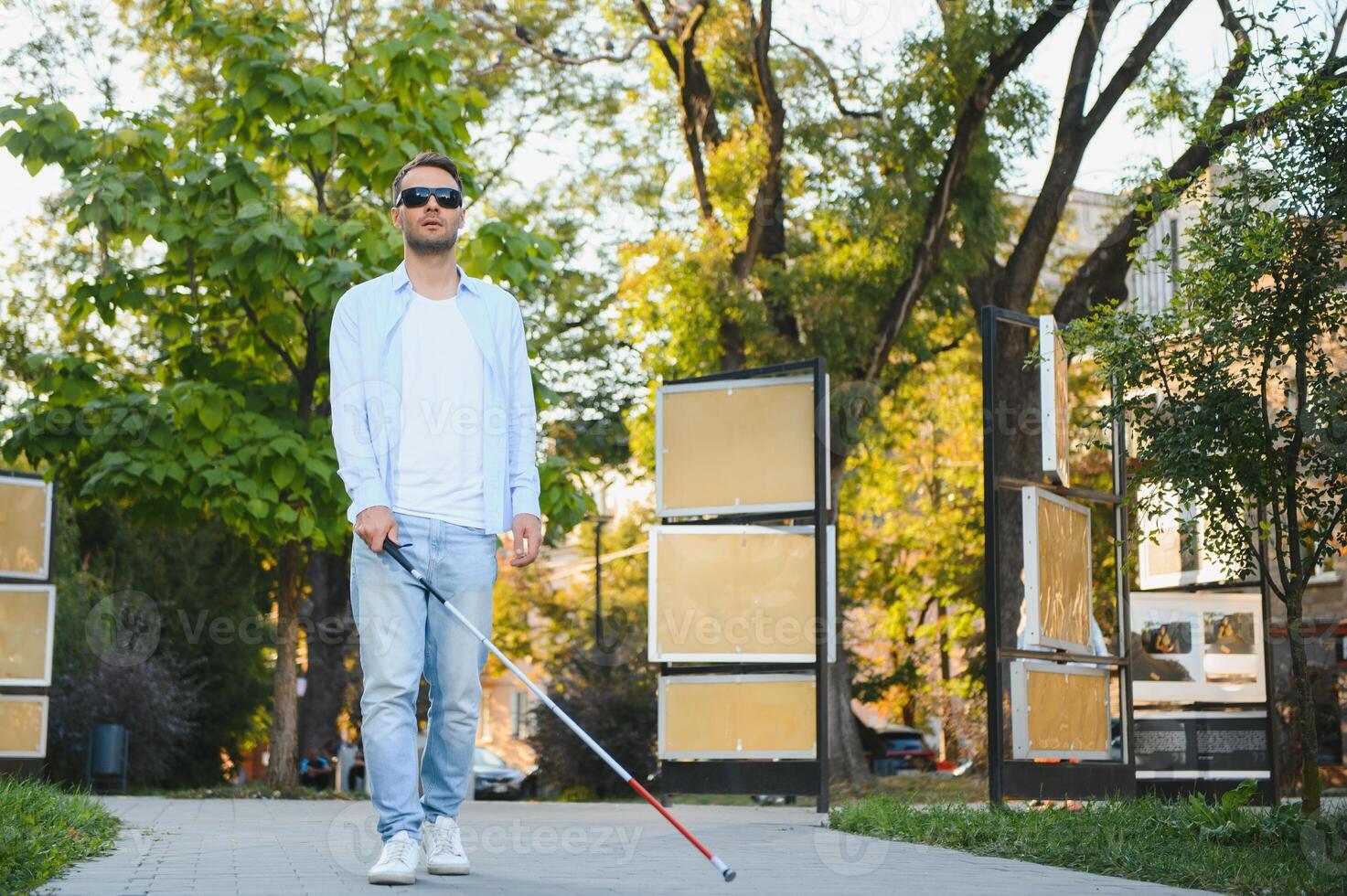 Young handsome blinded man walking with stick in town photo