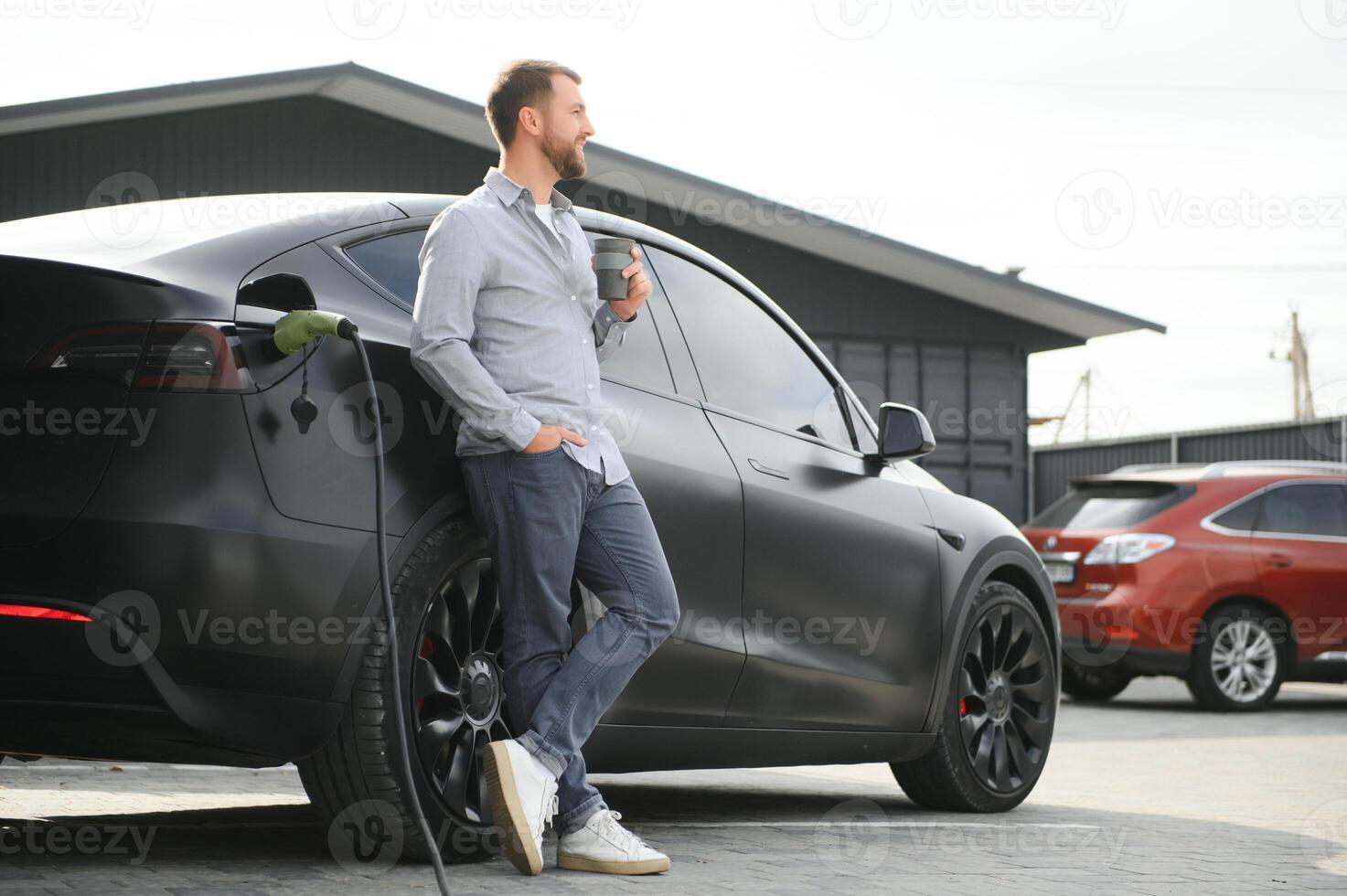 hermoso hombre Bebiendo café mientras cargando eléctrico coche foto