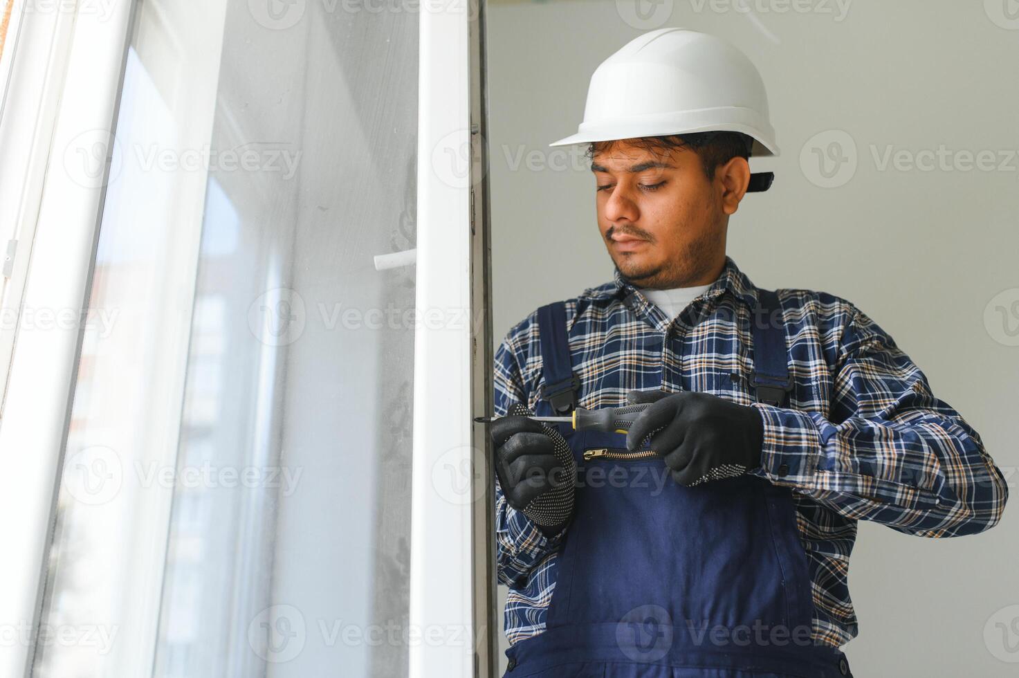 Indian Workman in overalls installing or adjusting plastic windows in the living room at home photo