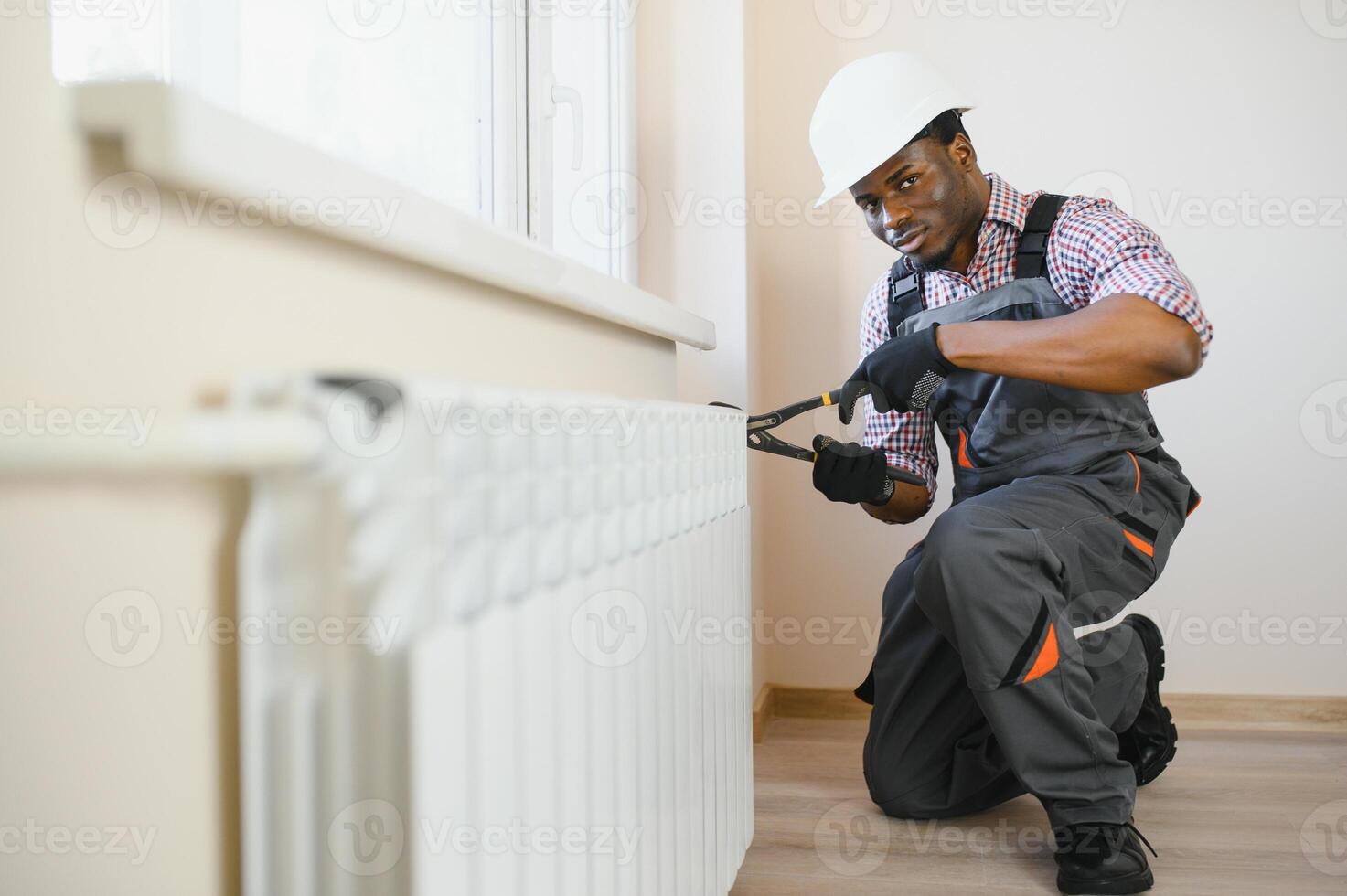 afro repairman in overalls using tools while installing or repairing heating radiator photo