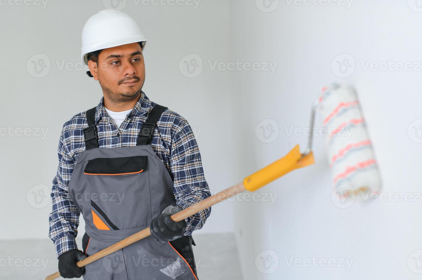 An Indian apartment repair worker paints a white wall with a roller. photo