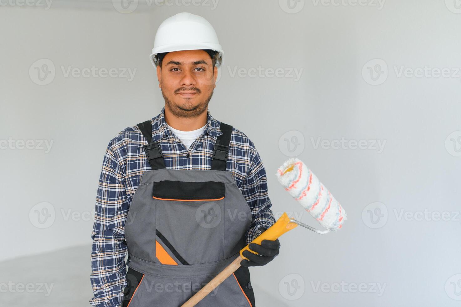 An Indian apartment repair worker paints a white wall with a roller. photo