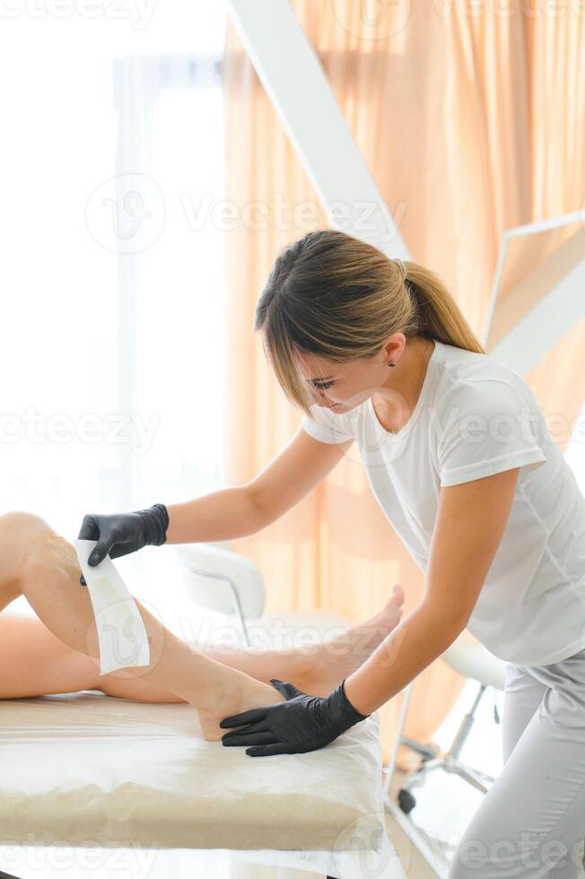 Beautician waxing female legs in spa center photo